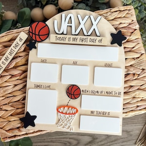 May include: A wooden sign with the name "JAXX" and the text "TODAY IS MY FIRST DAY OF". It features basketball-themed decorations, including a basketball, a hoop, and star accents. The sign includes spaces for date, age, weight, and other details.