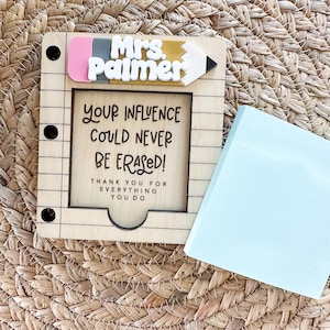 May include: A wooden notepad holder with the name "Mrs. Palmer" and a pencil design. The notepad holder has the text "YOUR INFLUENCE COULD NEVER BE ERASED! THANK YOU FOR EVERYTHING YOU DO." A light blue sticky note pad is next to the holder.