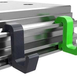 Peut inclure: Deux crochets en plastique, l'un noir et l'autre vert, sont fixés à une surface métallique. Les crochets sont conçus pour accrocher des objets.