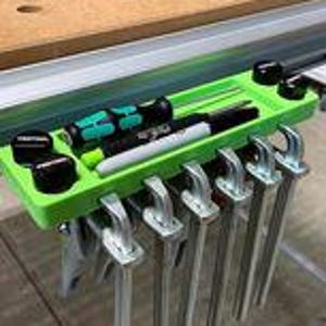 Peut inclure: Organisateur d'outils vert avec des boutons noirs et un plateau pour ranger les petits outils. L'organisateur est monté sur un établi et plusieurs pinces y sont suspendues.