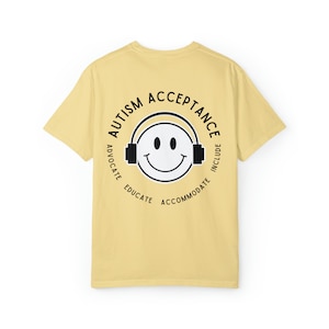 May include: A yellow t-shirt with a black circle graphic on the back. The graphic features a smiley face with headphones and the text "Autism Acceptance" around the outside. The text "Advocate, Educate, Accommodate, Include" is written around the inside of the circle.