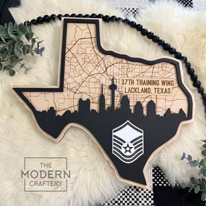 May include: A wooden cutout of the state of Texas with a black silhouette of the Dallas skyline and a white Air Force insignia. The text "37th Training Wing Lackland, Texas" is on the cutout.