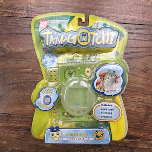 Peut inclure: Un kit Gotchi Gear Tama-decoratchi neuf et non ouvert dans son emballage d'origine. Le kit comprend un étui cool, des autocollants et des cristaux pour décorer un Tamagotchi. L'emballage est vert et jaune avec le logo et les illustrations de personnages Tamagotchi.