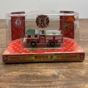 May include: A die-cast model fire engine in a clear display case. The model is red, white, and green with the number "99" on the side. The packaging reads "CODE 3 FIRE ENGINE" and "LIMITED EDITION".