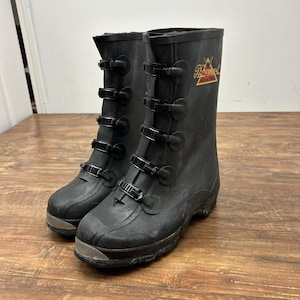 Puede incluir: Un par de botas de goma negras con múltiples correas de hebilla ajustables. Las botas tienen una puntera texturizada y un logotipo en la parte superior de la caña. Las botas están diseñadas para uso y protección en exteriores.