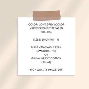 May include: A white paper with text about clothing sizes and materials, including "LIGHT GREY", "3MONTHS - YL", "BELLA + CANVAS JERSEY", and "GILDAN HEAVY COTTON". The paper is held by a piece of tape.