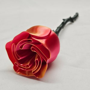 May include: A single red and orange rose with a black stem. The rose is made of plastic and has a shiny finish.