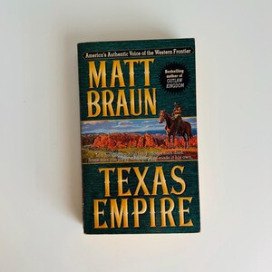 Pu&ograve; includere: Un libro con copertina rigida intitolato "Texas Empire" di Matt Braun. La copertina presenta un cowboy a cavallo contro un paesaggio desertico. Il titolo del libro e il nome dell'autore sono in lettere dorate su sfondo verde.