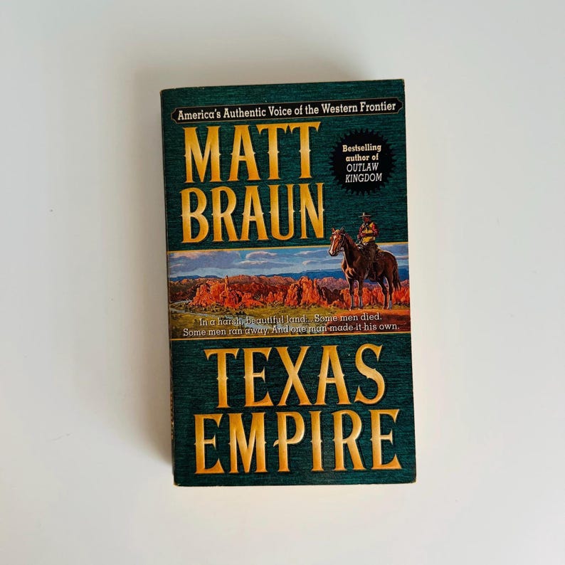 Pu&ograve; includere: Un libro con copertina rigida intitolato "Texas Empire" di Matt Braun. La copertina presenta un cowboy a cavallo contro un paesaggio desertico. Il titolo del libro e il nome dell'autore sono in lettere dorate su sfondo verde.
