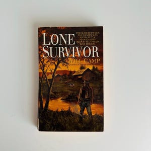 Pu&ograve; includere: Un libro tascabile intitolato "Lone Survivor" di Will Camp. La copertina presenta un'illustrazione a tema western con un uomo con un cappello, un paesaggio con un fiume e il testo "La guerra tra gli stati era finita, ma una faida sanguinaria antropofaga era appena iniziata."