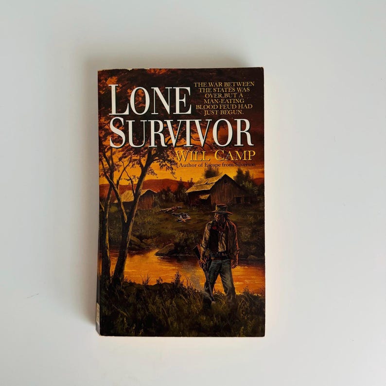 Pu&ograve; includere: Un libro tascabile intitolato "Lone Survivor" di Will Camp. La copertina presenta un'illustrazione a tema western con un uomo con un cappello, un paesaggio con un fiume e il testo "La guerra tra gli stati era finita, ma una faida sanguinaria antropofaga era appena iniziata."