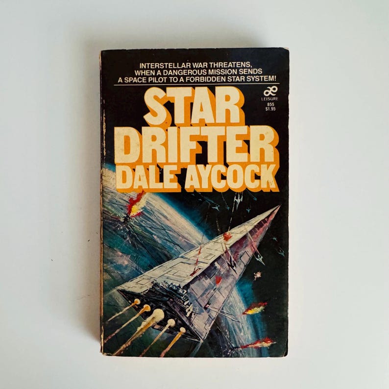 Pu&ograve; includere: Un libro tascabile vintage intitolato "Star Drifter" di Dale Aycock. La copertina presenta un'astronave che spara ad altre navi nello spazio, con il titolo in grandi lettere gialle. Lo sfondo &egrave; una scena spaziale blu scuro e verde.