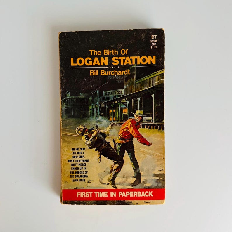 Pu&ograve; includere: Libro tascabile vintage intitolato "The Birth of Logan Station" di Bill Burchardt. La copertina presenta un'illustrazione a tema western di una sparatoria di fronte a un saloon. Il testo "First Time in Paperback" &egrave; in basso.