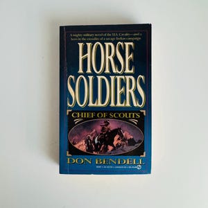 Pu&ograve; includere: Un libro tascabile intitolato "HORSE SOLDIERS" di Don Bendell. La copertina &egrave; prevalentemente blu con scritte bianche e dorate. Il sottotitolo del libro &egrave; "CHIEF OF SCOUTS" e presenta un'illustrazione di cavalieri in un paesaggio montuoso.