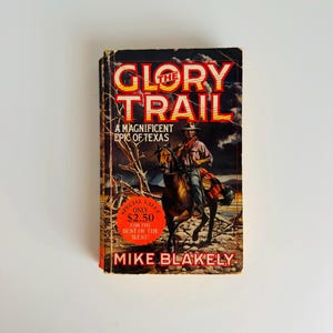 Pu&ograve; includere: Libro tascabile vintage intitolato "The Glory Trail" di Mike Blakely. La copertina presenta un cowboy a cavallo, con il titolo in grandi lettere arancioni. Il libro &egrave; una "Magnifica epopea del Texas".