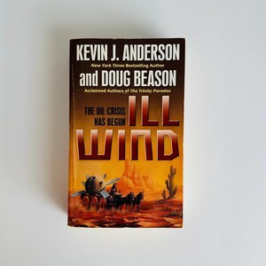 Pu&ograve; includere: Un libro tascabile intitolato "Ill Wind" di Kevin J. Anderson e Doug Beason. La copertina presenta un paesaggio desertico con un veicolo futuristico e il testo "The Oil Crisis Has Begun". Il libro ha uno schema di colori marrone e arancione.