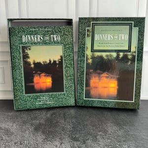 May include: A two-piece box set titled Sharon O'Connor's Dinners for Two, featuring a dark green border with a decorative pattern. The central image displays a house illuminated at night by a lake, with text indicating recipes and music.