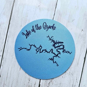 May include: A blue round coaster with a black outline of Lake of the Ozarks.