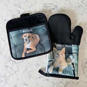 May include: A set of two black oven mitts with personalized images. One mitt features a brown and white dog named "Matthew" and the other mitt features two cats named "Scooby & Coupon".