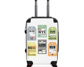 May include: A white rolling suitcase with black accents and a retractable handle. The suitcase is decorated with colorful travel tags from various cities, including NYC, London, and Dublin. The tags feature city names, flight details, and flag designs.