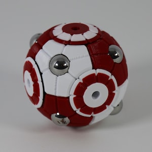 May include: A spherical puzzle toy with a red and white geometric design. The ball features a series of circular patterns and is held together by silver-colored magnetic spheres. The toy is designed to be manipulated and solved.