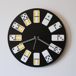 May include: A black and white domino clock with yellow, blue, green, and red dots. The clock face is black with white dominoes arranged in a circle around the clock hands.