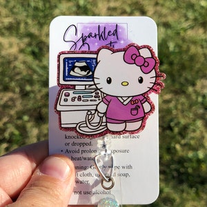 May include: Pink glitter Hello Kitty ultrasound technician retractable badge reel.  The reel features Hello Kitty in a pink scrub top, in front of an ultrasound machine. The card attached includes care instructions: Avoid prolonged heat/water exposure; Gently wipe with a soft cloth, mild soap, and water; Do not use alcohol.  The text 'Sparkled' is visible on the card.