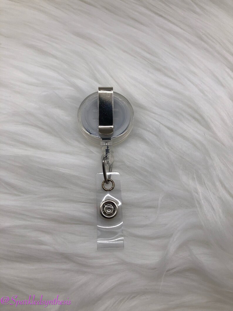 May include: A clear plastic retractable badge holder with a silver clip and a silver swivel hook. The holder has a clear plastic strap with a silver circle on it.