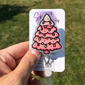 May include: A pink glitter Christmas tree with colorful lights, a white glitter background, and the text "Sparkly is" on a white card with a clear plastic badge holder.