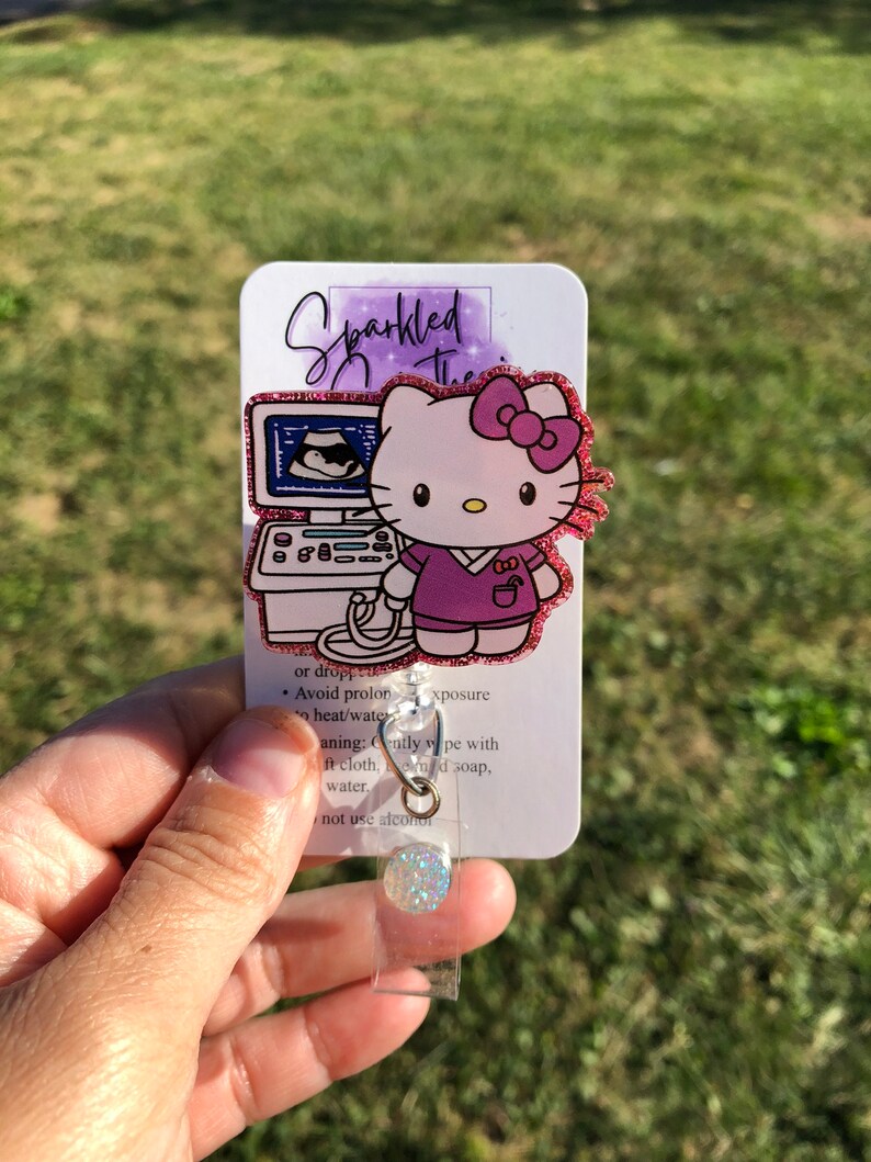 May include: A pink Hello Kitty character with a pink bow and a stethoscope, holding a pink ultrasound machine. The background is a watercolor-style design with the text "Sparkled The".