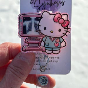 May include: Pink Hello Kitty character wearing a light blue scrub top with a pink flower on the pocket. The character is holding a pink and white medical device with an x-ray image on the screen. The text "Sparkled Synthesis" is at the top of the image.