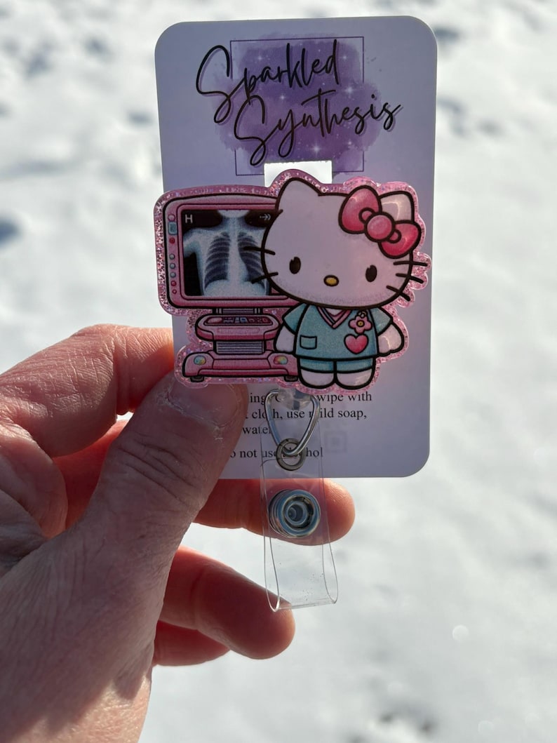 May include: Pink Hello Kitty themed badge holder with a glittery finish. The badge holder features Hello Kitty dressed as a doctor with a pink ultrasound machine. The text "Sparkled Synthesis" is printed on the back of the badge holder.