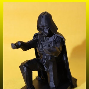 May include: A black 3D printed figurine of Darth Vader kneeling with his arms outstretched. The figurine is on a black base with the words "MADE IN USA" printed on it.