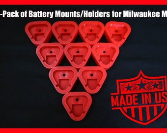 May include: Ten red plastic battery mounts for Milwaukee M12 tools. The mounts are arranged in a triangle shape. The text "MADE IN USA" is visible in the lower right corner of the image.