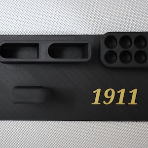 May include: Black plastic organizer with multiple compartments, including a long slot, a small rectangle, and a row of eight round holes. The text "1911" is printed in gold on the organizer.