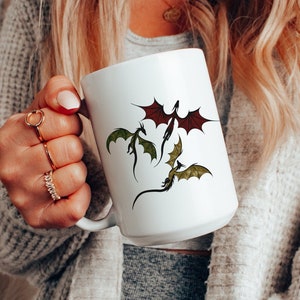 May include: White ceramic mug featuring a design of three dragons in flight. The dragons are green, red and black.