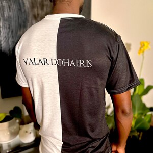 May include: A black and white t-shirt with the text "Valar Dohaeris" printed on the back. The shirt is split down the middle, with one side black and the other white.