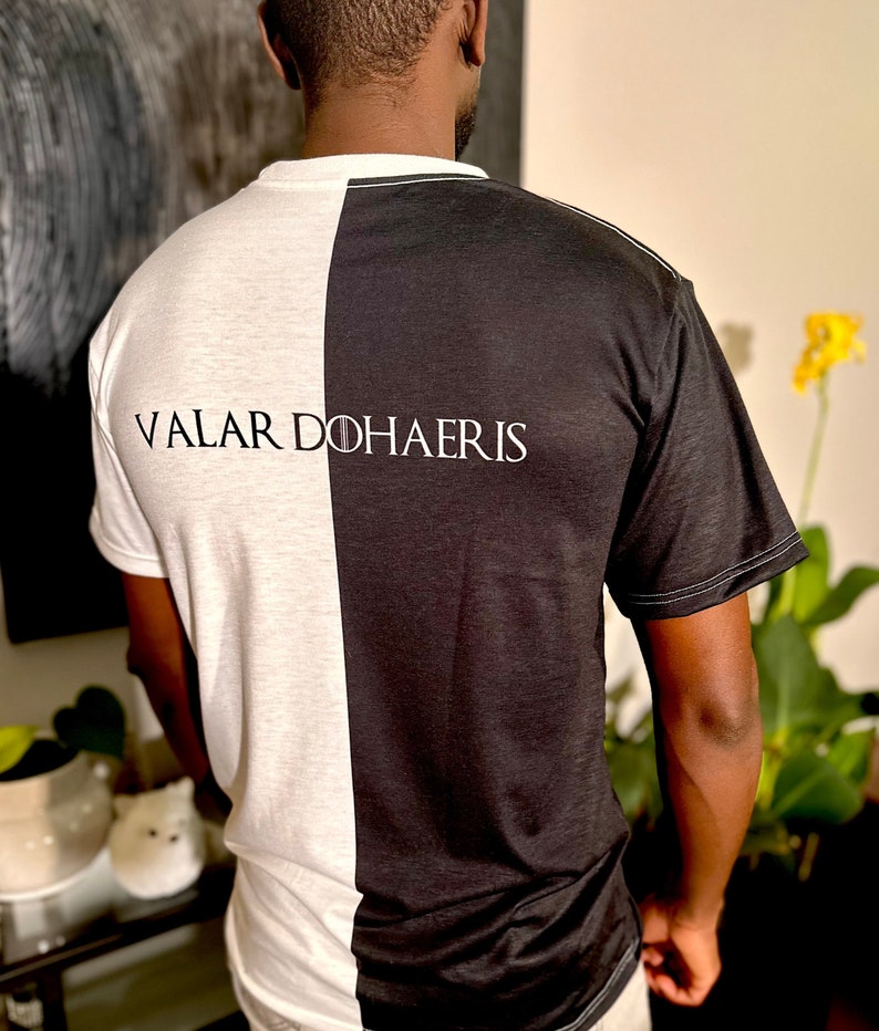 May include: A black and white t-shirt with the text "Valar Dohaeris" printed on the back. The shirt is split down the middle, with one side black and the other white.