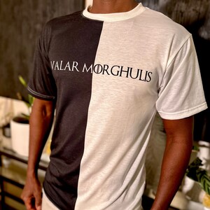 May include: A black and white t-shirt with the text "Valar Morghulis" printed on the front. The shirt is split down the middle, with one side black and the other white.