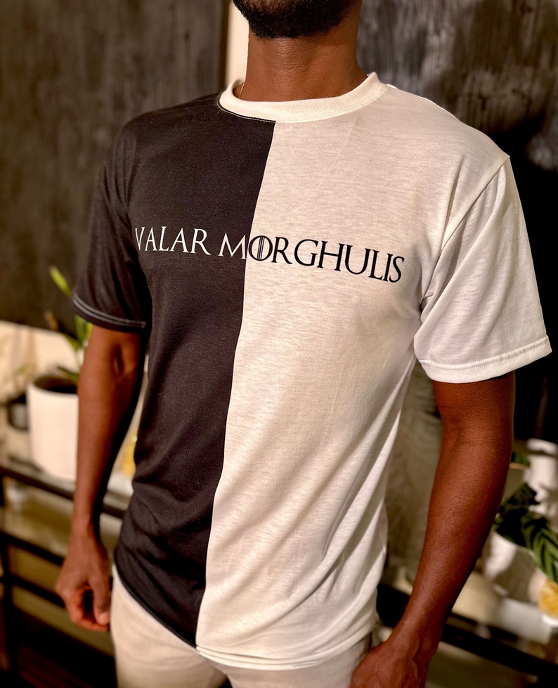 May include: A black and white t-shirt with the text "Valar Morghulis" printed on the front. The shirt is split down the middle, with one side black and the other white.