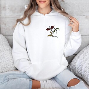 May include: White hoodie with a graphic of three dragons flying in a formation. The dragons are red, green, and black.