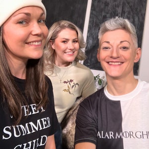 May include: Three people are wearing t-shirts with different designs. The person on the left is wearing a black t-shirt with the text "Sweet Summer Child". The person in the middle is wearing a light beige t-shirt with a design of three dragons. The person on the right is wearing a black and white t-shirt with the text "Alar Morghi".
