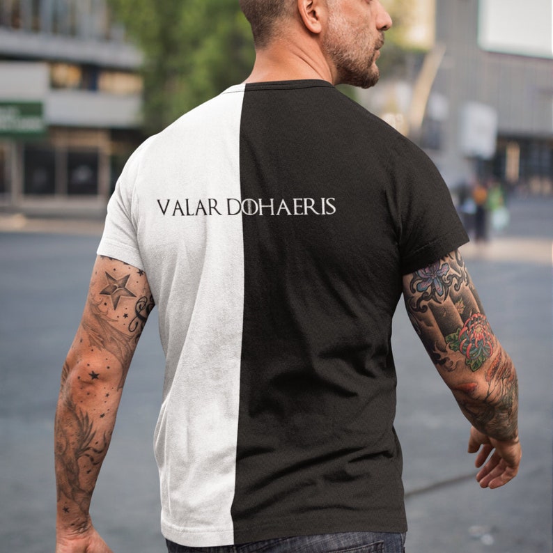 May include: A black and white t-shirt with the text "Valar Dohaeris" printed on the back. The shirt is split down the middle, with one side white and the other side black.
