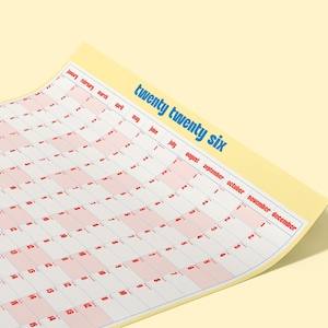 May include: A 2026 wall calendar with a yellow border and a grid of red and white squares. The text "twenty twenty six" is printed in blue. The months are listed along the top.