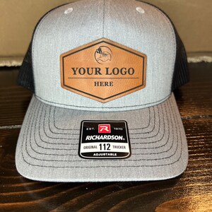 May include: Gray and black trucker hat with a brown leather patch that says "YOUR LOGO HERE" and a black label that says "EST. 1970 RICHARDSON. ORIGINAL 112 TRUCKER ADJUSTABLE"