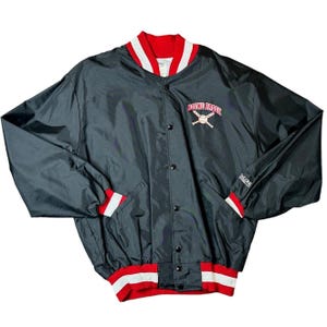 May include: Black baseball jacket with red and white accents. The jacket features the text "ROUND BROOK" in red with crossed baseball bats. The collar, cuffs, and hem have red and white striped detailing. The jacket has a button-up front and two pockets.