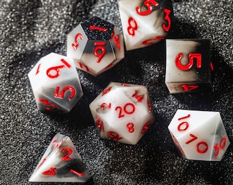 May include: A set of ten black and white dice with red numbers. The dice are in various positions on a black surface.
