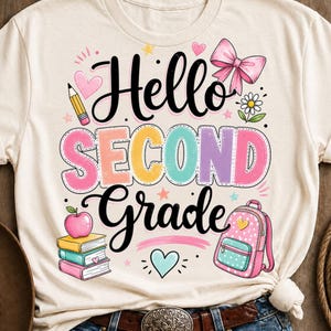May include: A cream-colored t-shirt featuring a graphic with the text Hello SECOND Grade in black and colorful block letters. The design includes illustrations of a yellow pencil, a pink bow, a daisy, a stack of three books, an apple, and a pink backpack.