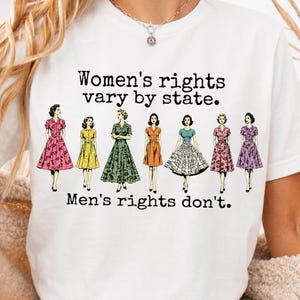 Könnte beinhalten: Ein weißes T-Shirt mit dem schwarzen Text "Women's rights vary by state. Men's rights don't." und einer grafischen Darstellung von sieben Figuren in Kleidern im Vintage-Stil in verschiedenen Farben wie Rosa, Gelb, Grün, Orange und Lila.
