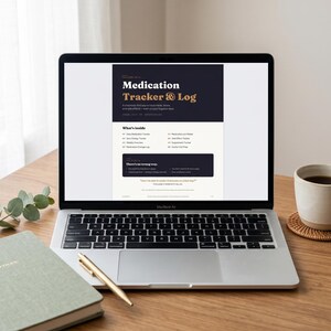 May include: A laptop showing a "Medication Tracker & Log" document sits on a wooden desk. The screen features a dark navy and cream design with headings and bullet points. A green notebook, a gold pen, and a coffee cup are also present.